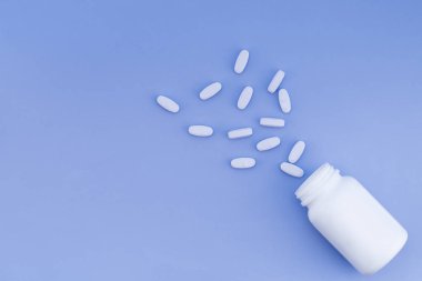 Bir şişe pastel mavi arka plan üzerinde dağınık hapları. Metin için yer. Düz yatıyordu.