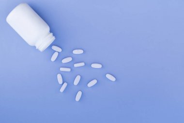 Parlak mavi bir arka plan üzerinde beyaz tabletler ve beyaz bir şişe yalıtılır. Tıp kavramı