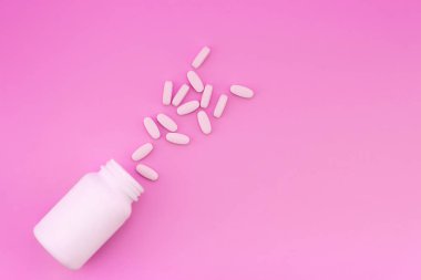 White tablets and a white bottle are isolated on a bright pink background. Medical concept clipart