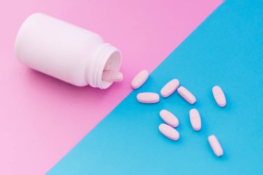Beyaz pembe ve mavi hap. Makro fotoğraf bir pastel renkli arka plan üzerinde beyaz bir şişe dışında o dökmek pills