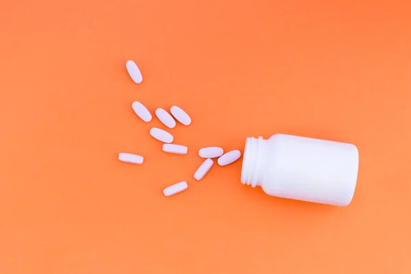 Piller är hällde ur en burk på en orange bakgrund. Vitaminer på ljusa rosa bakgrund. Ovanifrån. Flat Lay — Stockfoto