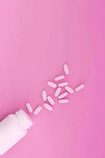 Piller hälls från en vit flaska på pastell rosa bakgrund. Plats för text. Lekmanna-platt. — Stockfoto