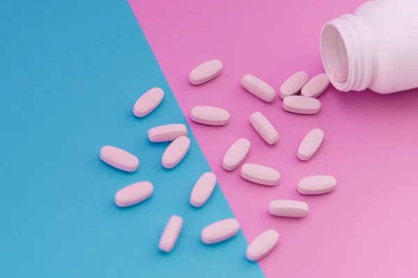 Makro foto av vita piller som hälla ut en flaska på en ljus blå och rosa bakgrund. Medicinska begrepp — Stockfoto