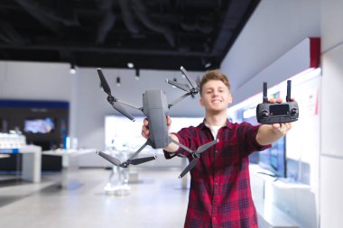 Olumlu bir genç adam bir quadcopter elleri ve bir kontrol paneli deponun arka planda tutar. Adam bir davul ve bir konsol sunmaktadır. Bir dron bir teknoloji mağaza satın