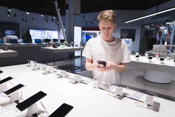 Un hermoso estudiante con una camiseta blanca mira a los teléfonos inteligentes en t —  Fotos de Stock