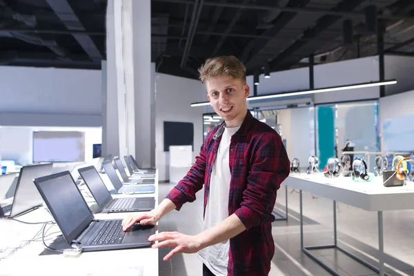 Un joven compra un portátil en una tienda de tecnología. Retrato de una p —  Fotos de Stock