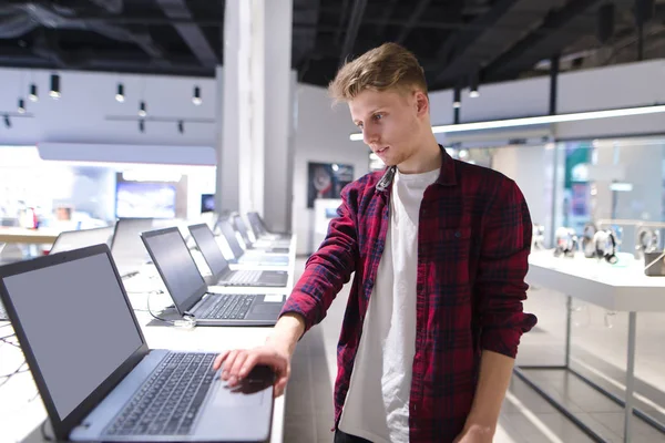 Un joven comprador hermoso elige un ordenador portátil en una electrónica moderna —  Fotos de Stock