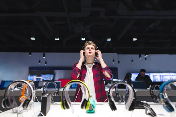 Un joven elige un auricular en una tienda moderna. Prueba de auriculares . —  Fotos de Stock