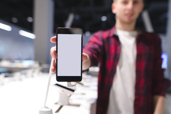 A man in a red shirt shows a smartphone with a white screen. A smartphone in the electronics store