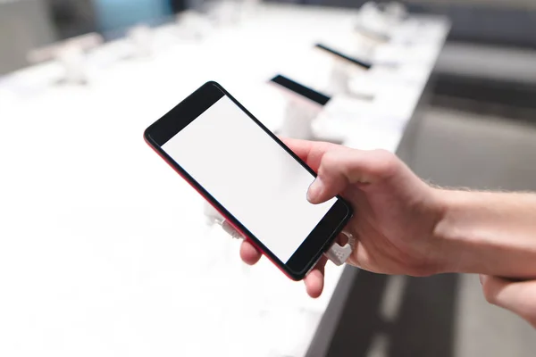 Sebuah tangan dengan smartphone di toko ponsel. Sebuah layar putih. Seorang pria memilih smartphone di toko — Stok Foto