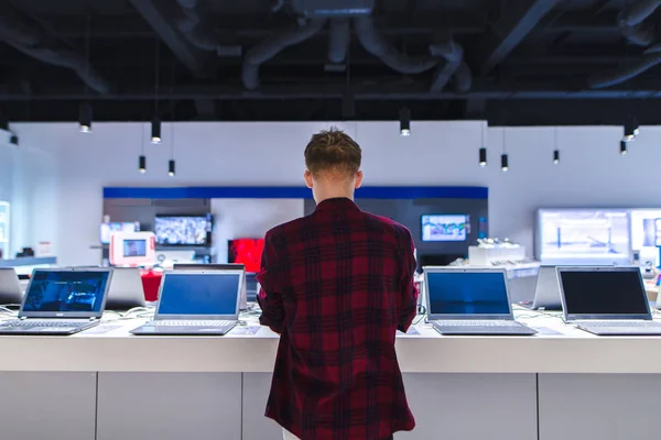 Ein junger Mann steht hinter seinem Laptop im Elektronikgeschäft. Ein junger Mann sucht sich im Laden einen Laptop aus — Stockfoto