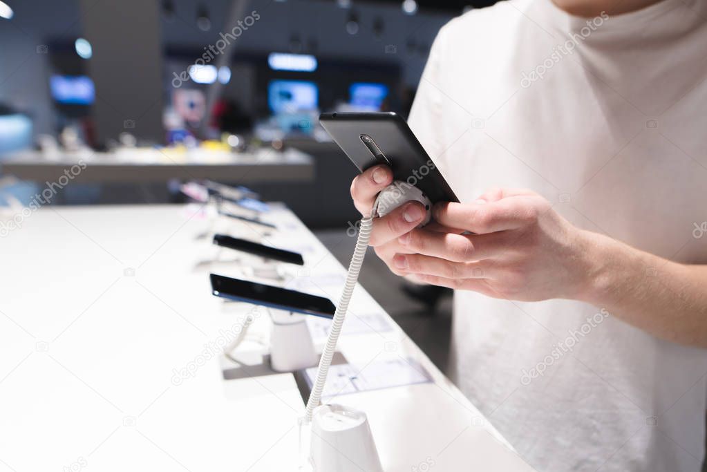 Choosing a smartphone in the electronics store. Man's hands test the phone in the store. Buy a smartphone in the tech store.