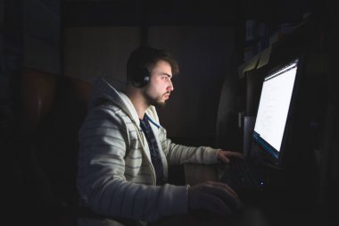 Sakal ve kulaklık ile genç bir adam, geceleri için Internet'i kullanır. Evde iş bilgisayar geceleri