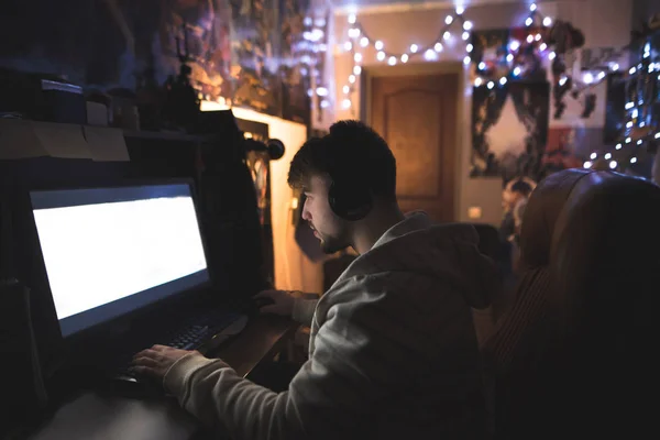 Een jonge man speelt computergames thuis in zijn kamer. Gamer zit op de computer in de avond in het gezellige kamer en speelt spelletjes — Stockfoto