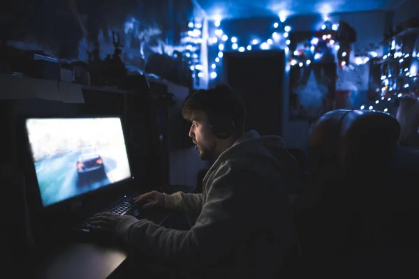 Здивований молодий чоловік грає в ігри на комп'ютері. Чоловік з бородою і навушниками грає гонку на комп'ютері — стокове фото
