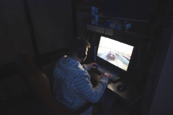 Gamer plays games at home on a computer. A man with headphones on his head plays a game of night at the computer