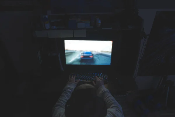 Een man speelt spelletjes bij nacht op een computer. Gamer speelt wedstrijden thuis. De handen op het toetsenbord bepalen hoe het spel verloopt. Gamer concept. — Stockfoto