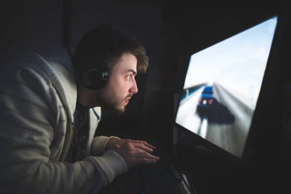 Концентрированный геймер сидит за монитором и играет в компьютерные игры. Молодой человек играет в наушники на компьютере. Концепция геймера . — стоковое фото