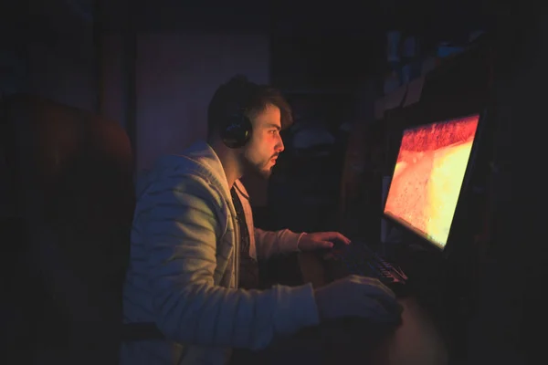 Ein niedlicher männlicher Spieler sitzt in einem gemütlichen Raum hinter einem Computer und spielt — Stockfoto