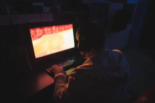 Um jogador focado senta-se no computador em casa no quarto aconchegante e — Fotografia de Stock