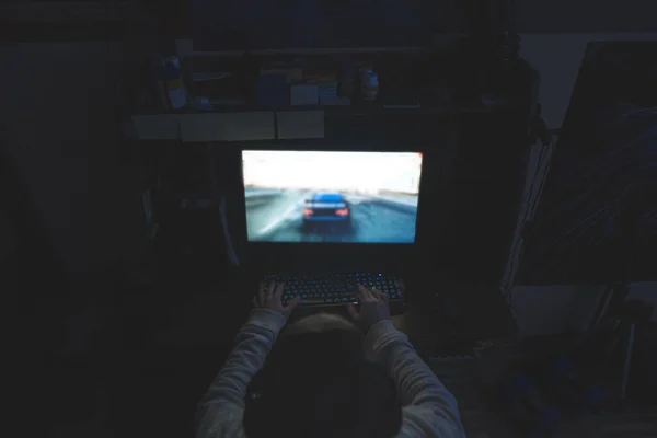 Un hombre juega por la noche en una computadora. Gamer juega carreras en casa. Las manos en el teclado controlan el proceso del juego. Concepto de jugador . — Foto de Stock