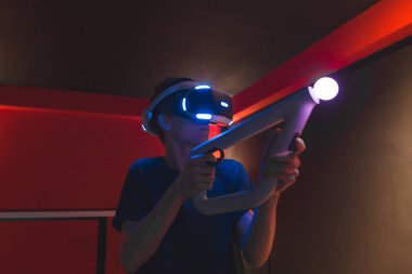 Gamer in the headset of virtual reality and the controller in his hands stands in a dark room and plays video games. Games at home with a VR headset