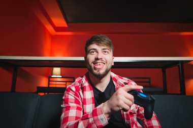 Mutlu oyun onun el ve gülümsüyor gamepad ile kanepede oturuyor. Bir sakallı bir adam bir kırmızı iç ile bir odada bir konsol oyunu oynar