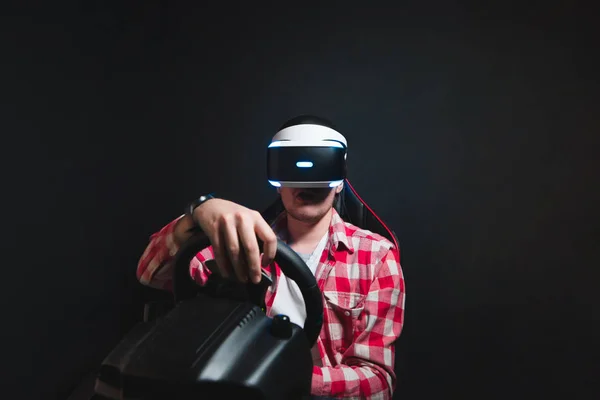 Ten hraje závod na simulátoru auta v virtuální realita brýle. Mladý muž hraje Vr her na černém pozadí. — Stock fotografie