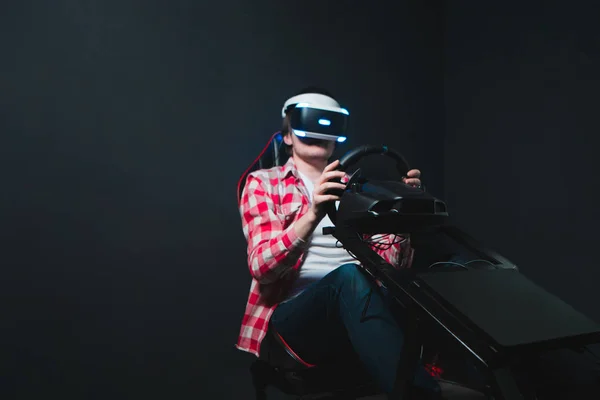 Gamer joue la course sur le simulateur de voiture dans le casque VR. Jeux vidéo dans le casque VR. Les courses informatiques du futur. Un homme joue à des jeux en réalité virtuelle sur fond noir . — Photo