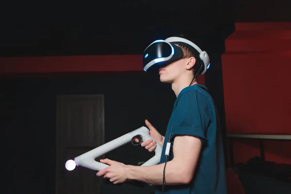 Jeune homme joue dans les jeux de tir en utilisant des lunettes VR et un contrôleur. Un joueur avec un casque VR est à la maison dans la salle et joue à des jeux vidéo. Concept de réalité visuelle . — Photo