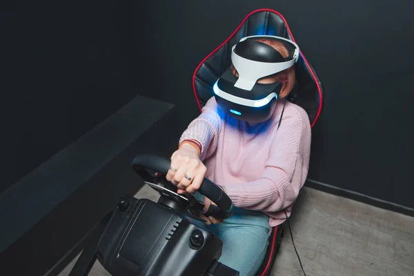 Une jeune fille joue une course VR avec un casque de réalité virtuelle sur la tête dans un simulateur de voiture. Concept de réalité virtuelle. Jeux réalistes — Photo