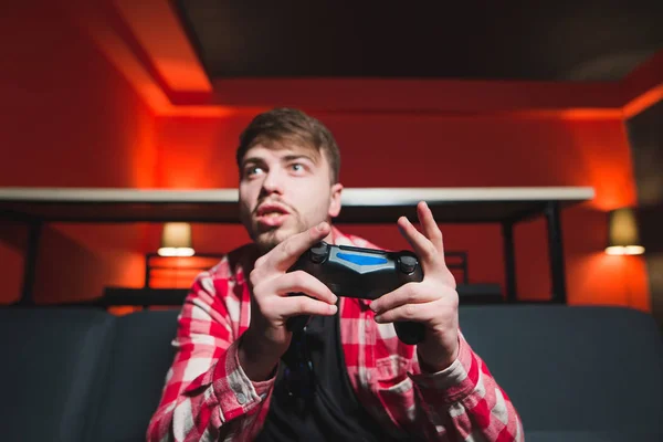 An expressive young man with a gamepad in his hands plays video games at home on the console. Portrait of the gamer behind the game on the console