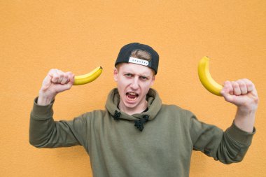 Muz onun elinde olan duygusal bir genç adam bir turuncu duvar arka plan üzerinde duruyor ve kameraya benziyor