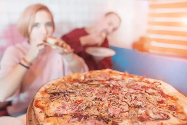 Leckere Pizza auf dem Hintergrund eines jungen Paares. ein Paar, das in einem Café eine Pizza isst. Pizza steht im Fokus, die Menschen sind verschwommen. Platz für Text. — Stockfoto
