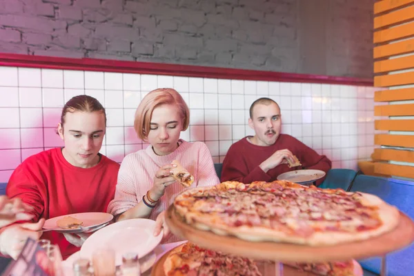 Los estudiantes se sientan en una acogedora pizzería y comen una deliciosa pizza. Pizza de almuerzo con amigos. Un encuentro de jóvenes en la pizzería —  Fotos de Stock