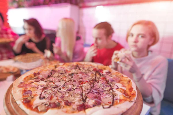 A delicious large pizza in the pizzeria, against the background of a group of young people. Students eat pizza in a cozy restaurant