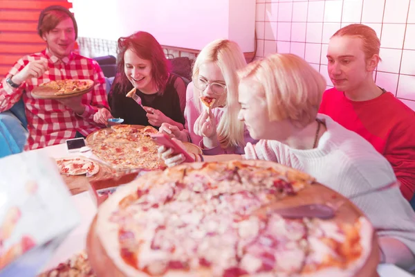 Jovens felizes estão sentados em um restaurante e comendo pizza grande. Um grupo de amigos positivos comendo pizza deliciosa em uma pizzaria aconchegante. Fim de semana com amigos e pizza — Fotografia de Stock