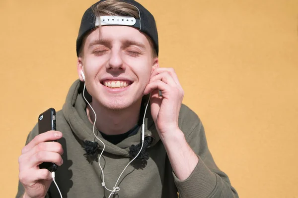 El joven cerró los ojos mientras escuchaba música en los auriculares. Un estudiante está escuchando música sobre un fondo naranja. Primer plano . — Foto de Stock