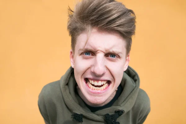 Portrait d'un jeune garçon malveillant près d'un mur orange. Un jeune homme en colère et drôle regarde la caméra — Photo