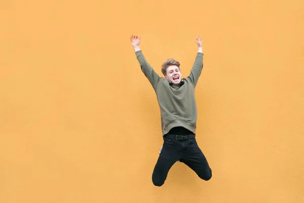 Молодой человек в повседневной одежде прыгает на фоне оранжевой стены. Эмоциональный прыжок счастливого человека на цветном фоне . — стоковое фото