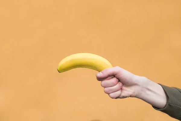 La mano dell'uomo tiene una banana sullo sfondo di una parete arancione. Copyspace — Foto Stock