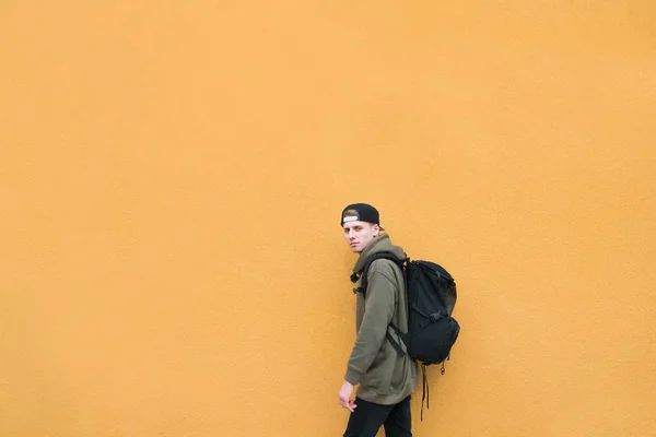 유행 거리 젊은 남자는 배낭에 큰 오렌지 벽의 배경에 서 있다. Copyspace. — 스톡 사진