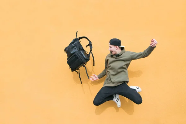 Ulicy młody człowiek skoki z plecakiem na tle muru pomarańczowy — Zdjęcie stockowe