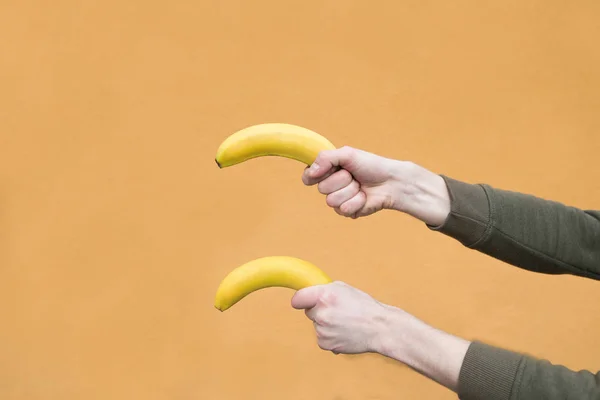 Due mani di uomini tengono due banane sullo sfondo di una parete arancione — Foto Stock