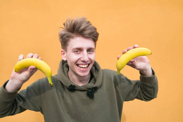 Portrait of a smiling young man with bananas in his hands on an orange background. A look at the camera