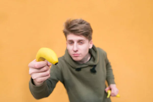 Сосредоточься на банане. Забавный парень держит в руках банан и смотрит в камеру. . — стоковое фото