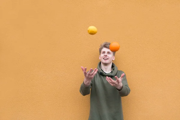 Χαρούμενος νεαρός juggles με πορτοκάλι και λεμόνι φόντο έναν πορτοκαλί τοίχο. — Φωτογραφία Αρχείου