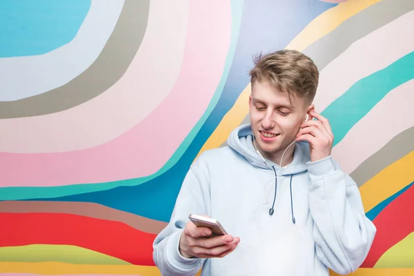 Щасливий молодий чоловік використовує смартфон і налаштовує навушники на студійному кольоровому фоні — стокове фото