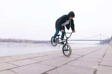 BMX freestyle. A young man is doing tricks on a BMX bike near the river clipart