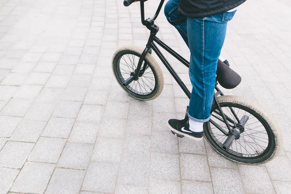 Un giovane uomo in jeans guida una bici BMX in città. Gambe e bici da vicino — Foto Stock